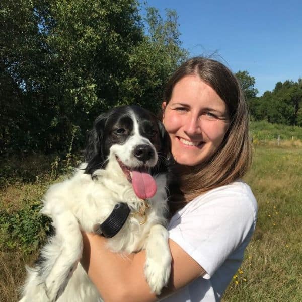 Katharina K. aus dem Website-team hat einen Hund auf dem Arm und guckt in die Sonne.