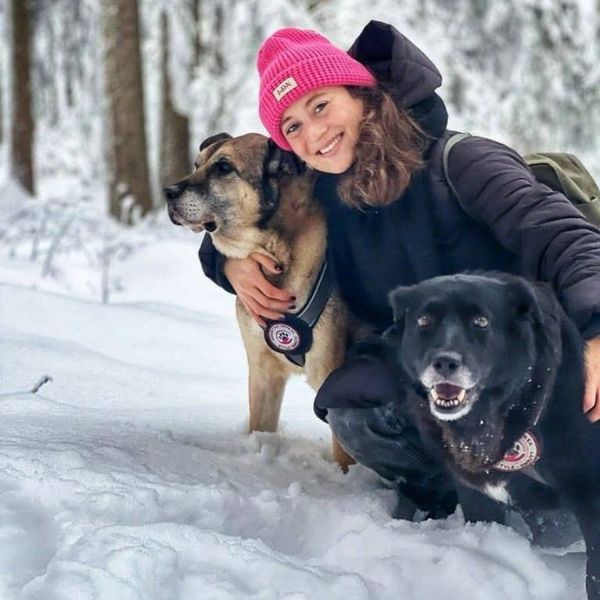 Frau mit zwei Hunden im Wald im Schnee.