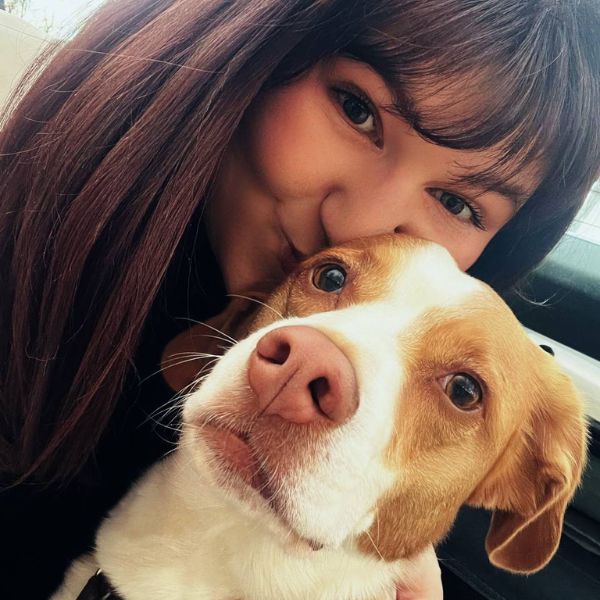 Frau mit braunen Haaren und einem braun,weißen Hund schaut in die Kamera.