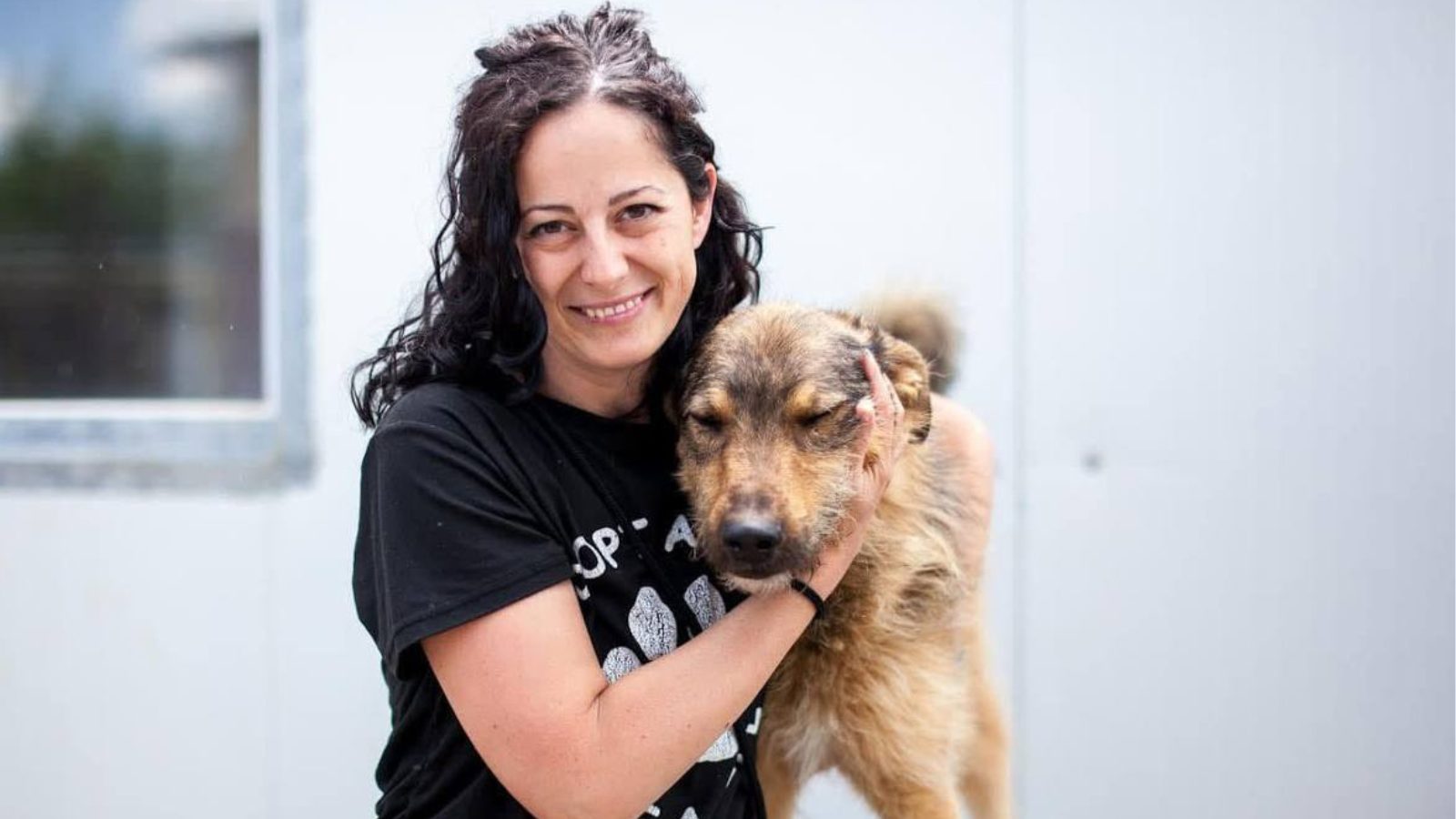 Frau mit schwarzen Haaren steht neben einem Hund und schaut in die Kamera