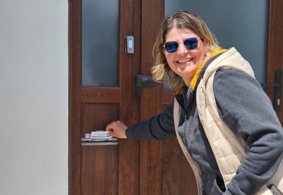 Frau steckt einen Brief in einen Briefkasten an einer Tür