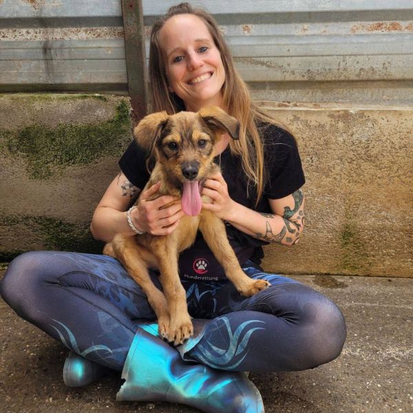Frau sitzt mit einem Hund auf dem Schoß und schaut in die Kamera