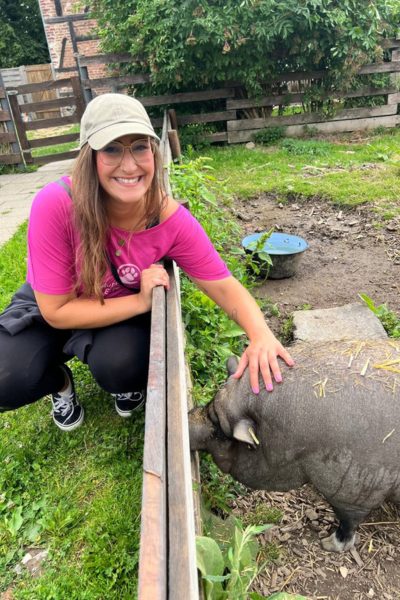 Frau streichelt Schwein und schaut in die Kamera.