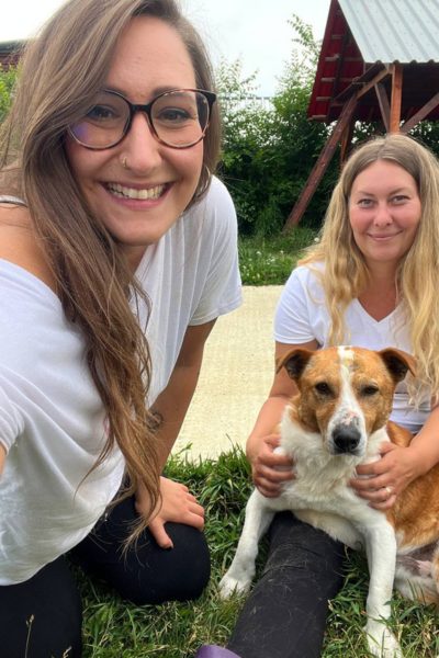 Zwei Frauen mit Hund schauen in die Kamera.