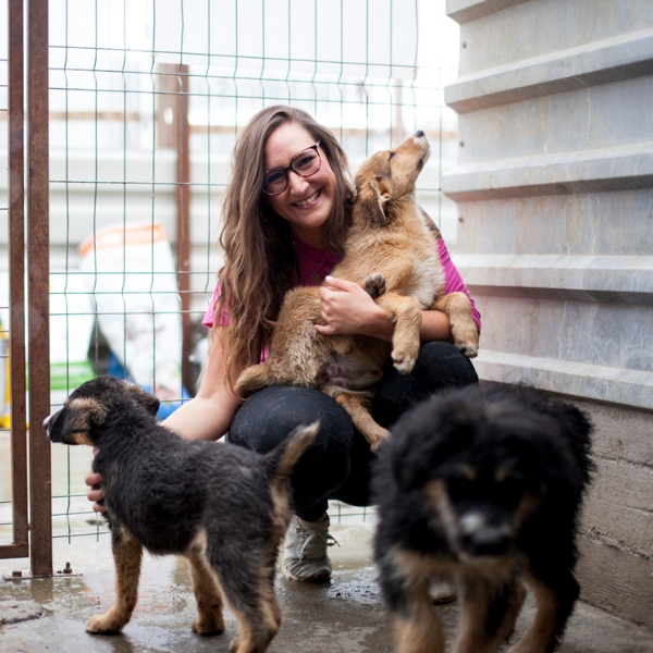 Frau mit Hunden in einem Zwinger schaut in die Kamera.