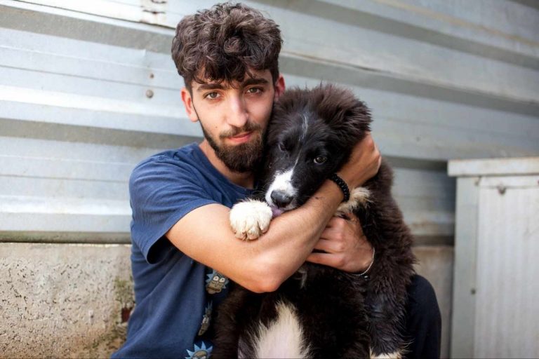 Tierpfleger Ionut knuddelt einen schwarzen Hund