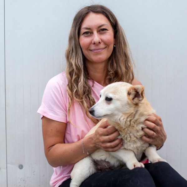 Frau mit Hund auf dem Schoß schaut in die Kamera