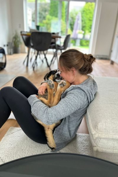 Frau sitzt mit einem schwarz-braunen Hund auf dem Schoß