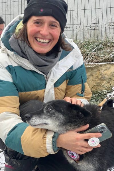 Laurene lacht in die Kamera und hält einen schwarzen Hund im Arm