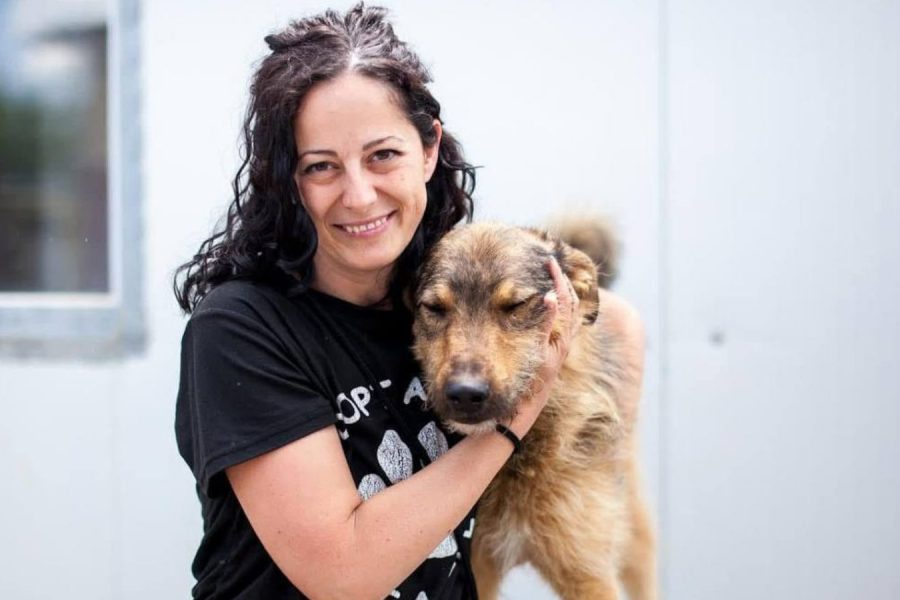 Frau mit schwarzen Haaren steht neben einem Hund und schaut in die Kamera