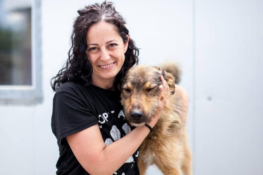 Frau mit schwarzen Haaren steht neben einem Hund und schaut in die Kamera