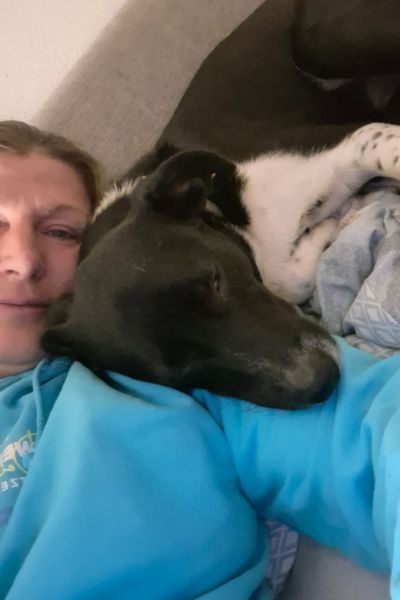 Ein Hund und eine Frau liegen beieinander und schauen in die Kamera.